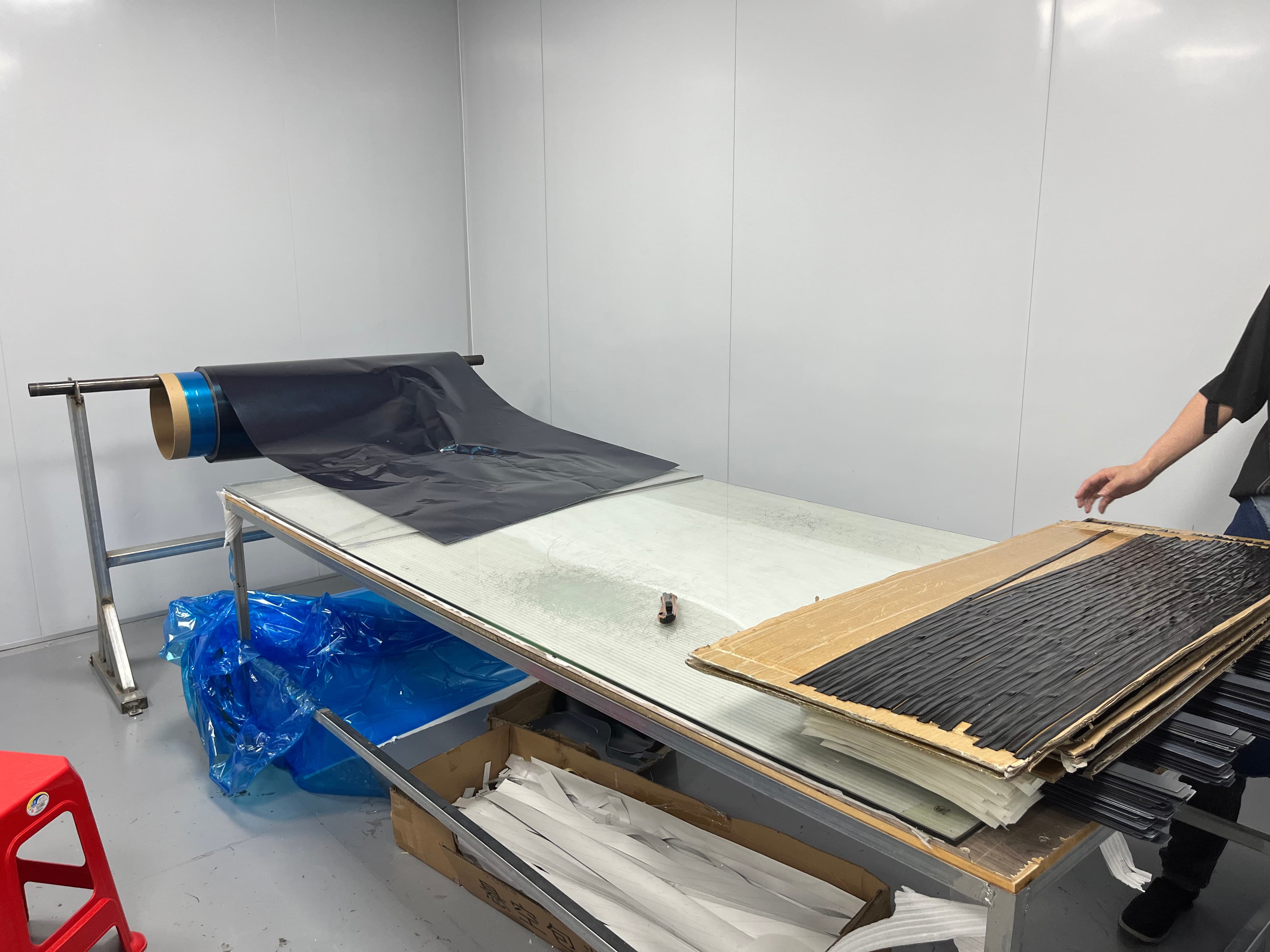 Dark material sheet spread across a factory worktable, with cut material arranged beside it