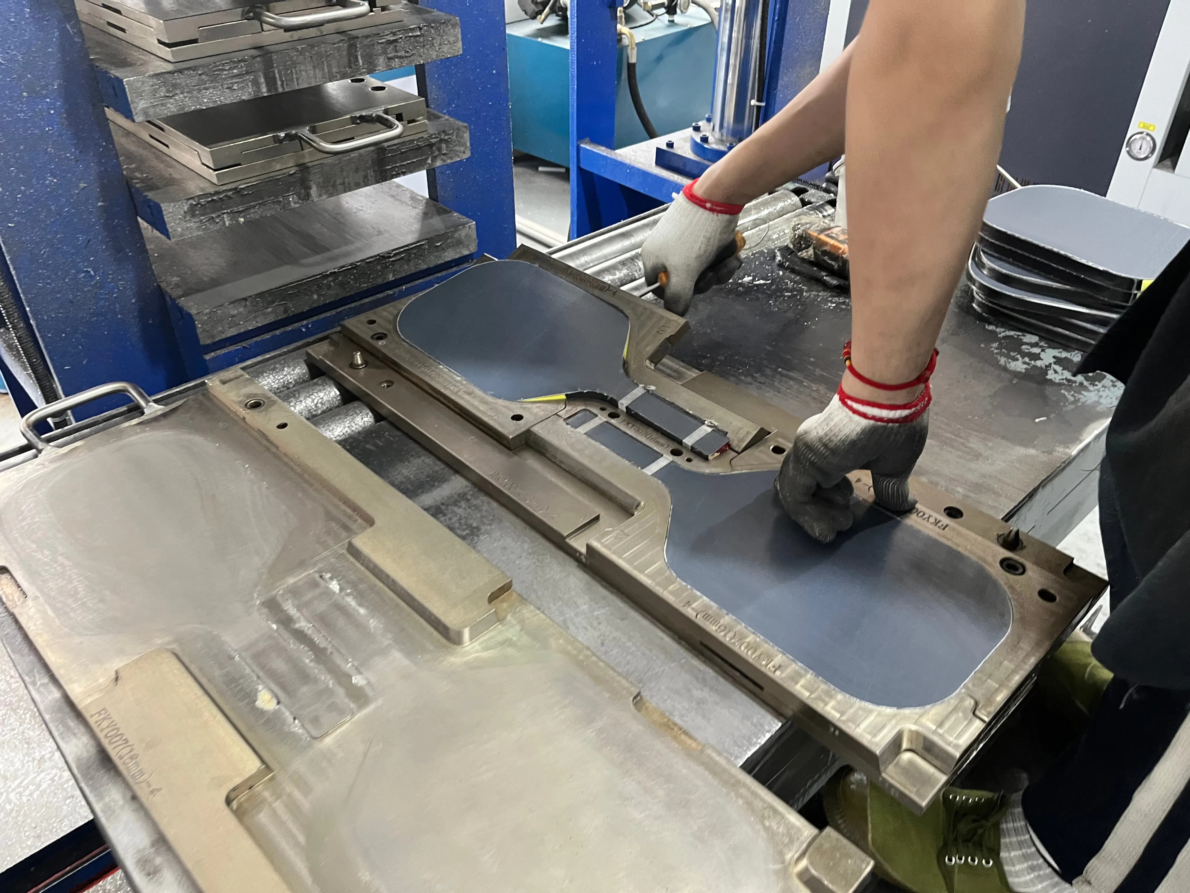 Worker forming a pickleball paddle in a hot press mold