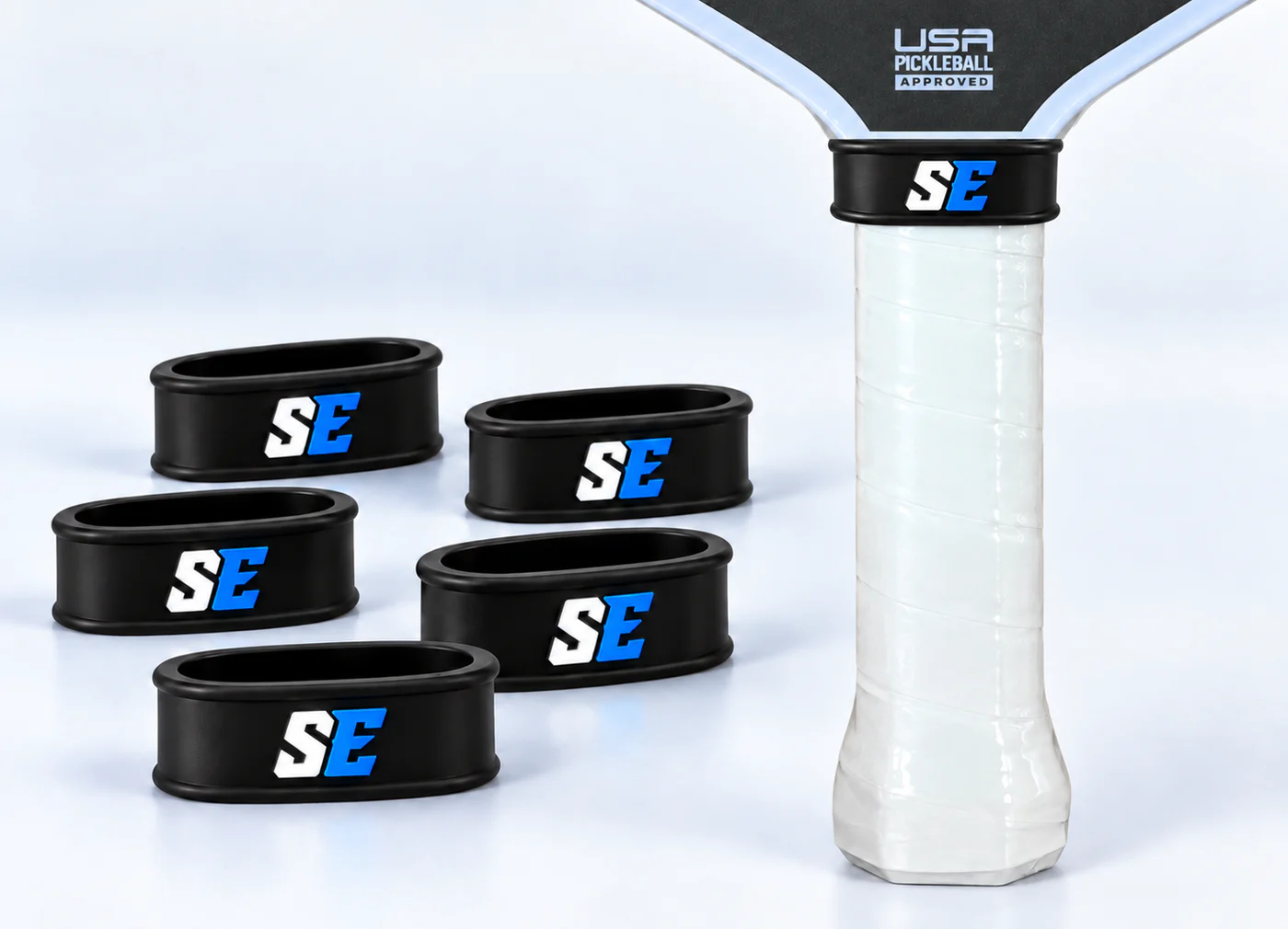 Small custom logo rubber rings installed at the upper transition of a real white pickleball paddle handle